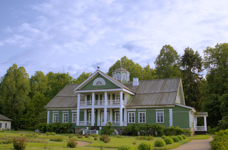 Green country house with a symmetrical structure, white columns, and high roof, set against a vibrant blue sky. Traditional architecture evokes the feeling of peaceful village lifeの写真素材