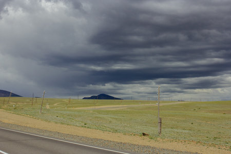 Expansive steppe landscape with power lines, stormy skies and mountains of Altay, capturing the calm before a summer rainstorm. Rural scene with open place and plainsの写真素材