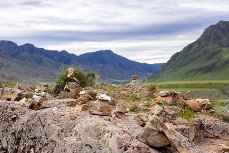 Scenic mountain landscape of Altai, rocky terrain and stone piles against cloudy sky, natural travel background. Stacked stones on mountain rocks with panoramic view of green valleys and high peaksの写真素材