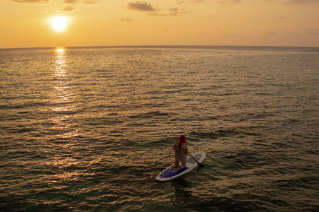 Aerial view of paddleboarder moving across glowing ocean water. Adventure travel scene, calm waves...