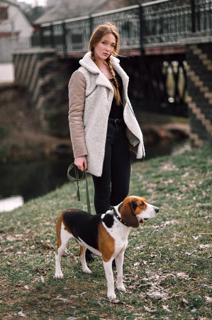 Young hipster girl with her pet estonian hound dog playing and having fun outdoor in the park.の写真素材