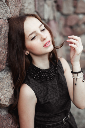 beautiful sad young woman on a stone wall background posing in a black dress, very sensual and emotionalの写真素材