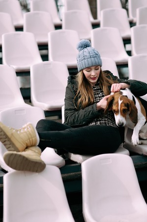 Young hipster girl with her pet estonian hound dog playing and having fun outdoor in the park. Fans at the stadiumの写真素材