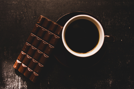 Cup of coffee with grains and chocolate on wooden table on dark backgroundの写真素材