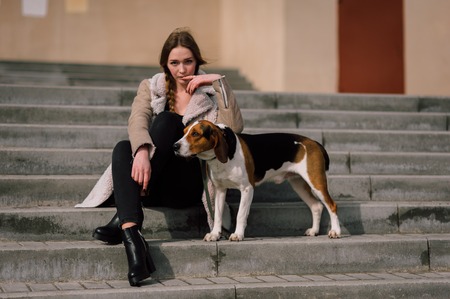 Young hipster girl with her pet estonian hound dog playing and having fun outdoor in the park.の写真素材