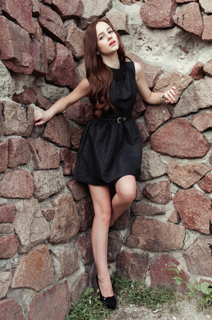 beautiful sad young woman on a stone wall background posing in a black dress, very sensual and emotionalの写真素材
