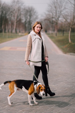 Young hipster girl with her pet estonian hound dog playing and having fun outdoor in the park.の写真素材