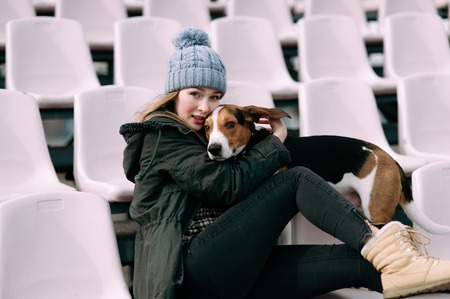 Young hipster girl with her pet estonian hound dog playing and having fun outdoor in the park. Fans at the stadiumの写真素材
