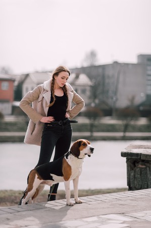 Young hipster girl with her pet estonian hound dog playing and having fun outdoor in the park.の写真素材