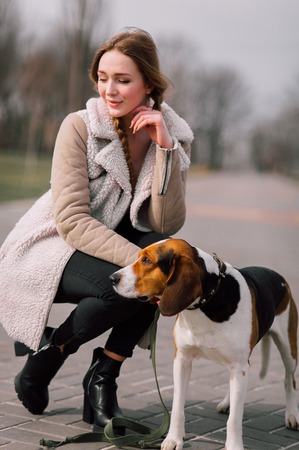 Young hipster girl with her pet estonian hound dog playing and having fun outdoor in the park.の写真素材