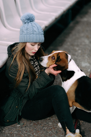 Young hipster girl with her pet estonian hound dog playing and having fun outdoor in the park.の写真素材