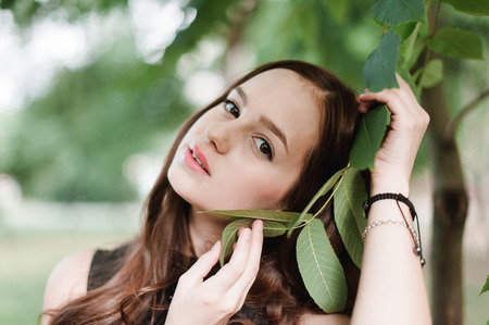 Beautiful young girl in black dress with long hair, super cute and natural standing among colorful green leavesの写真素材