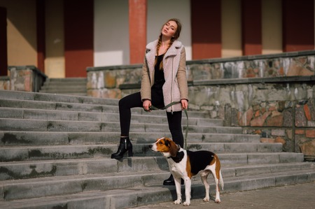 Young hipster girl with her pet estonian hound dog playing and having fun outdoor in the park.の写真素材
