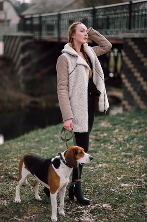 Young hipster girl with her pet estonian hound dog playing and having fun outdoor in the park.の写真素材