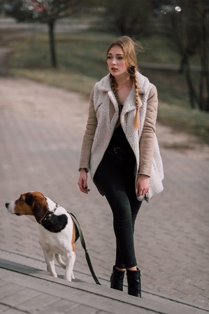 Young hipster girl with her pet estonian hound dog playing and having fun outdoor in the park.の写真素材
