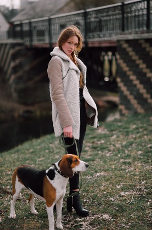Young hipster girl with her pet estonian hound dog playing and having fun outdoor in the park.の写真素材