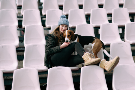 Young hipster girl with her pet estonian hound dog playing and having fun outdoor in the park. Fans at the stadiumの写真素材