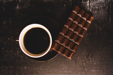 Cup of coffee with grains and chocolate on wooden table on dark backgroundの写真素材