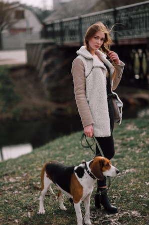 Young hipster girl with her pet estonian hound dog playing and having fun outdoor in the park.の写真素材
