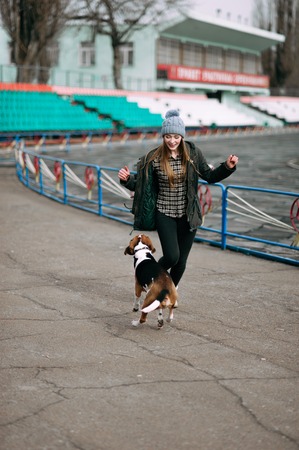 Young hipster girl with her pet estonian hound dog playing and having fun outdoor in the park.の写真素材