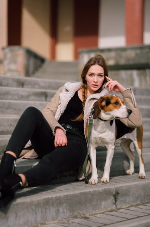 Young hipster girl with her pet estonian hound dog playing and having fun outdoor in the park.の写真素材
