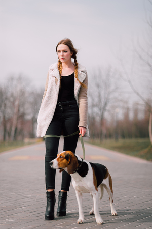 Young hipster girl with her pet estonian hound dog playing and having fun outdoor in the park.の写真素材