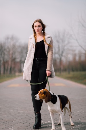 Young hipster girl with her pet estonian hound dog playing and having fun outdoor in the park.の写真素材
