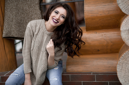 Spring in the country style. Full length portrait of young woman in white knitted sweater and furry hat standing in the front of rustic wood wall in the yard near house, wearing sweaterの写真素材