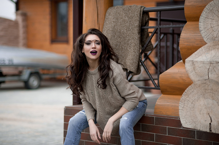 Spring in the country style. Full length portrait of young woman in white knitted sweater and furry hat standing in the front of rustic wood wall in the yard near house, wearing sweaterの写真素材