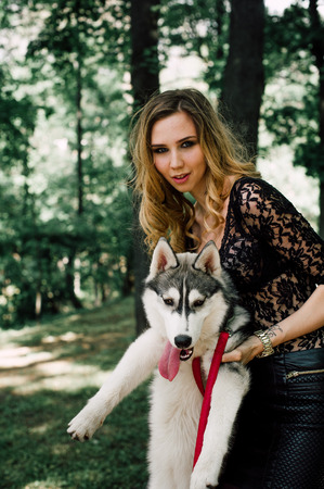 Girl in the park with a dog Husky. The girl with the siberian husky. Delightful girl plays with a Siberian Husky. Girl walking with a hunting dog - the West Siberian husky. Close-up. Fashion photoの写真素材