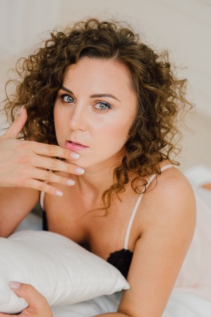 Sexy woman in bed in the morning showing her beautiful body. She doesn't wants to wake up. Awaken with natural light in her bedroom and covered with the bed sheets.の写真素材