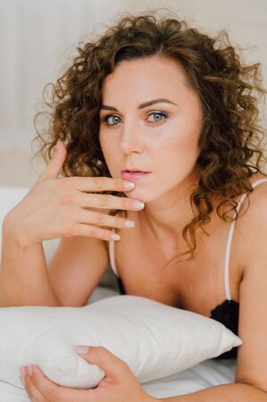 Sexy woman in bed in the morning showing her beautiful body. She doesn't wants to wake up. Awaken with natural light in her bedroom and covered with the bed sheets.の写真素材