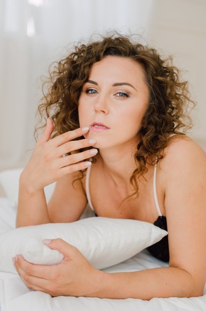 Sexy woman in bed in the morning showing her beautiful body. She doesn't wants to wake up. Awaken with natural light in her bedroom and covered with the bed sheets.の写真素材