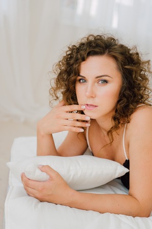 Sexy woman in bed in the morning showing her beautiful body. She doesn't wants to wake up. Awaken with natural light in her bedroom and covered with the bed sheets.の写真素材
