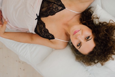Sexy woman in bed in the morning showing her beautiful body. She doesn't wants to wake up. Awaken with natural light in her bedroom and covered with the bed sheets.の写真素材