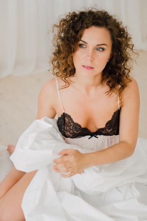 Sexy woman in bed in the morning showing her beautiful body. She doesn't wants to wake up. Awaken with natural light in her bedroom and covered with the bed sheets.の写真素材