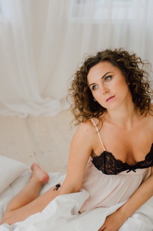 Sexy woman in bed in the morning showing her beautiful body. She doesn't wants to wake up. Awaken with natural light in her bedroom and covered with the bed sheets.の写真素材