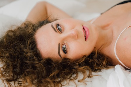 Sexy woman in bed in the morning showing her beautiful body. She doesn't wants to wake up. Awaken with natural light in her bedroom and covered with the bed sheets.の写真素材