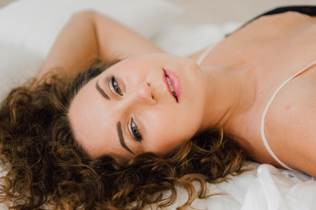 Sexy woman in bed in the morning showing her beautiful body. She doesn't wants to wake up. Awaken with natural light in her bedroom and covered with the bed sheets.の写真素材