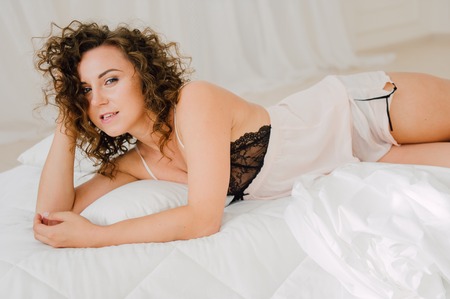 Sexy woman in bed in the morning showing her beautiful body. She doesn't wants to wake up. Awaken with natural light in her bedroom and covered with the bed sheets.の写真素材