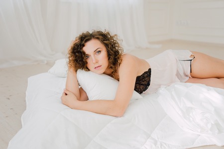 Sexy woman in bed in the morning showing her beautiful body. She doesn't wants to wake up. Awaken with natural light in her bedroom and covered with the bed sheets.の写真素材