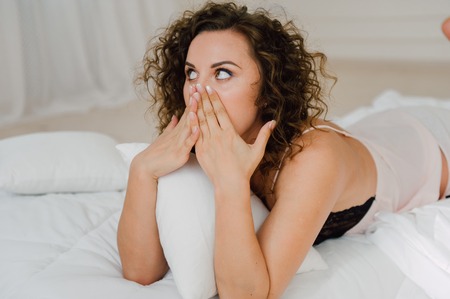 Sexy woman in bed in the morning showing her beautiful body. She doesn't wants to wake up. Awaken with natural light in her bedroom and covered with the bed sheets.の写真素材