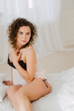 Sexy woman in bed in the morning showing her beautiful body. She doesn't wants to wake up. Awaken with natural light in her bedroom and covered with the bed sheets.の写真素材