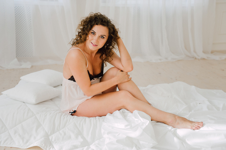 Sexy woman in bed in the morning showing her beautiful body. She doesn't wants to wake up. Awaken with natural light in her bedroom and covered with the bed sheets.の写真素材