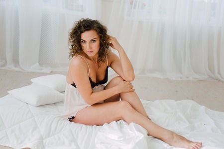 Sexy woman in bed in the morning showing her beautiful body. She doesn't wants to wake up. Awaken with natural light in her bedroom and covered with the bed sheets.の写真素材
