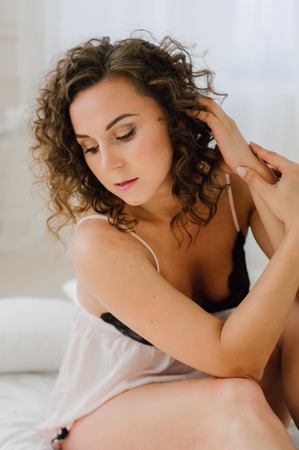 Sexy woman in bed in the morning showing her beautiful body. She doesn't wants to wake up. Awaken with natural light in her bedroom and covered with the bed sheets.の写真素材