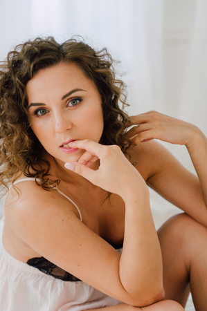 Sexy woman in bed in the morning showing her beautiful body. She doesn't wants to wake up. Awaken with natural light in her bedroom and covered with the bed sheets.の写真素材