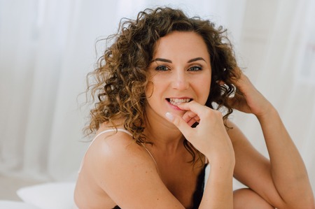 Sexy woman in bed in the morning showing her beautiful body. She doesn't wants to wake up. Awaken with natural light in her bedroom and covered with the bed sheets.の写真素材