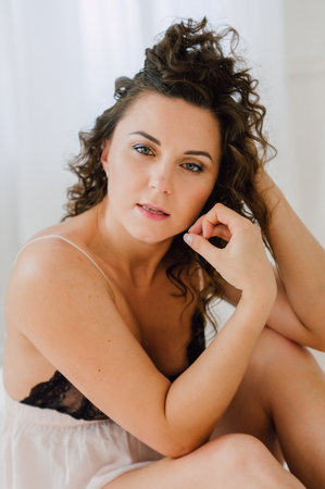 Sexy woman in bed in the morning showing her beautiful body. She doesn't wants to wake up. Awaken with natural light in her bedroom and covered with the bed sheets.の写真素材