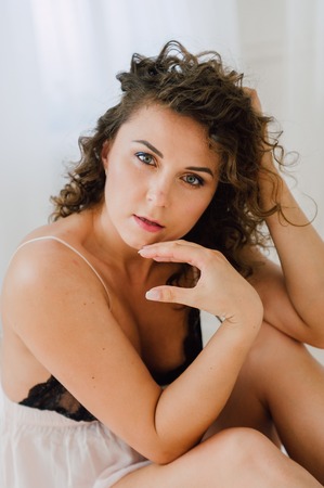 Sexy woman in bed in the morning showing her beautiful body. She doesn't wants to wake up. Awaken with natural light in her bedroom and covered with the bed sheets.の写真素材